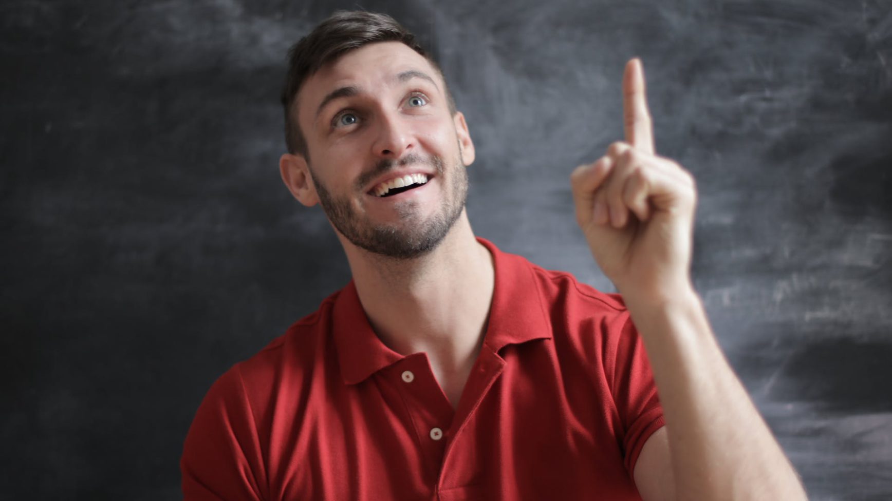 man in a red collared tshirt, smiling, looking up, and pointing up