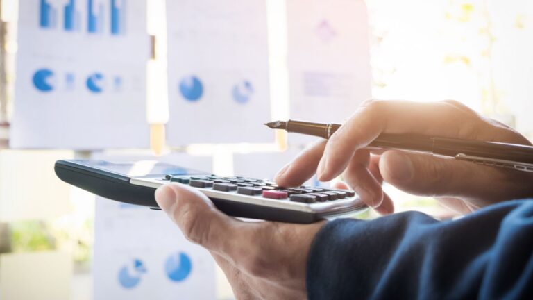 person holding a calculator in their left hand and a pen in their right, actively typing numbers