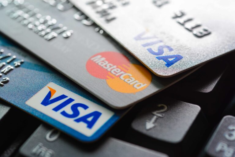 A close-up image of several stacked credit cards, including Visa and MasterCard, placed on a computer keyboard